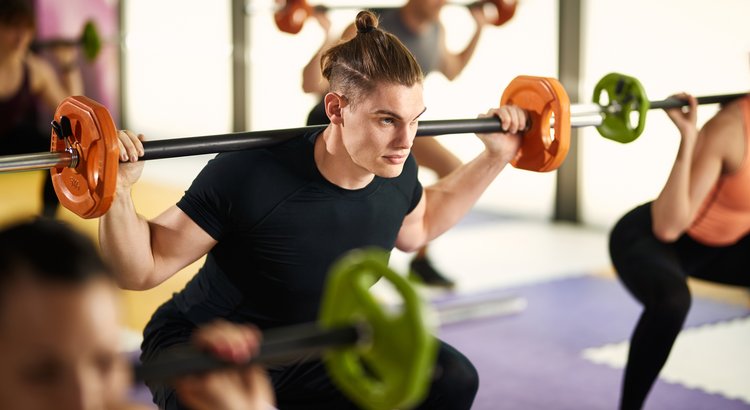 A focused trainer mid-set with a barbell in a well-equipped gym